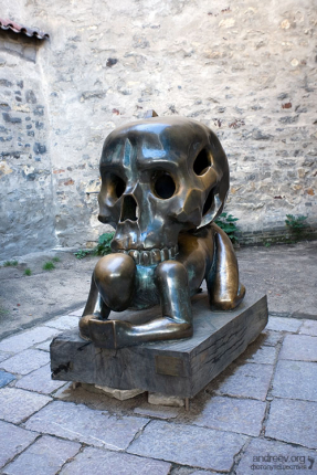 Скульптура бронзового человека, придавленного черепом. Расположена в тупике, в конце Златой улочки.