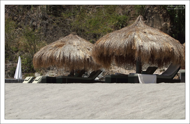 Лежаки и зонтики из тростника на черном вулканическом пляже Ансе Частанет.