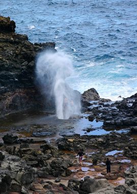 Люди, пробирающиеся через лаву к фонтану Nakalele blowhole.