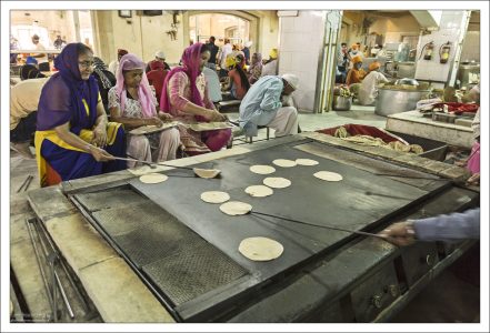 Волонтеры бросают лепешки на большие металлические листы над газовыми горелками, тесто тут же надувается шаром и резко опадает. Двое бросают, остальные ловко переворачивают «блины» с помощью металлических прутьев.