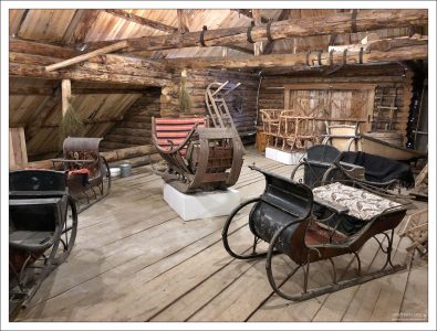 К магазину примыкал деревенский гараж. В нем мы видим сразу несколько основных типов крестьянских саней. Старейшие сани-пошевни в виде лодочки выставлены по центру на подиуме. А еще – выездные, парадные, плетеные, дровенки, сани-розвальни – для перевозки хозяйственных предметов. В былые времена все они активно использовались в хозяйстве в крестьянских домах.