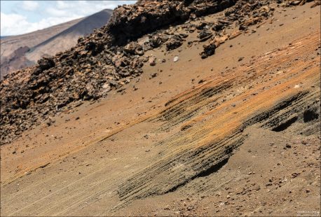 Рыжие склоны острова Бартоломе — следствие окисленных минералов в вулканической лаве. Молодые поля лавы часто покрыты тонким слоем пепла, песка или шлака, который может быть красновато-оранжевого цвета. Этот пепел создаёт «тёплый» оттенок склона, особенно на солнце.