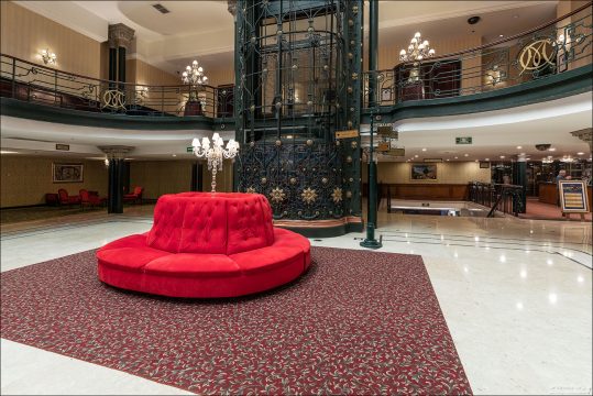 На первом этаже Gran Hotel Ciudad de México расположена нижняя станция исторического панорамного лифта, каркас которого украшен сложным кованым узором с позолоченными элементами. Перед ним установлена круглая вельветовая софа, дополняющая аутентичный интерьер вековой давности.