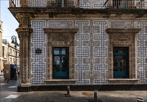 Детальный ракурс стены дворца Casa de los Azulejos демонстрирует геометрический узор из бело-голубых изразцов с жёлтыми акцентами. Оконные проемы и угловые пилястры здания украшены сложной резьбой по серому камню в стиле ультрабарокко (чурригереско).