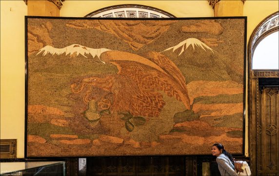 Картина из почтовых марок: Монументальное панно в холле Дворца почты, изображающее герб Мексики — орла, пожирающего змею на кактусе, на фоне заснеженных вулканов. Эта уникальная мозаика создана художником Пабло Маганьей Гонсалесом и выложена вручную из более чем 34 тысяч подлинных почтовых марок периода с 1890 по 1934 год.